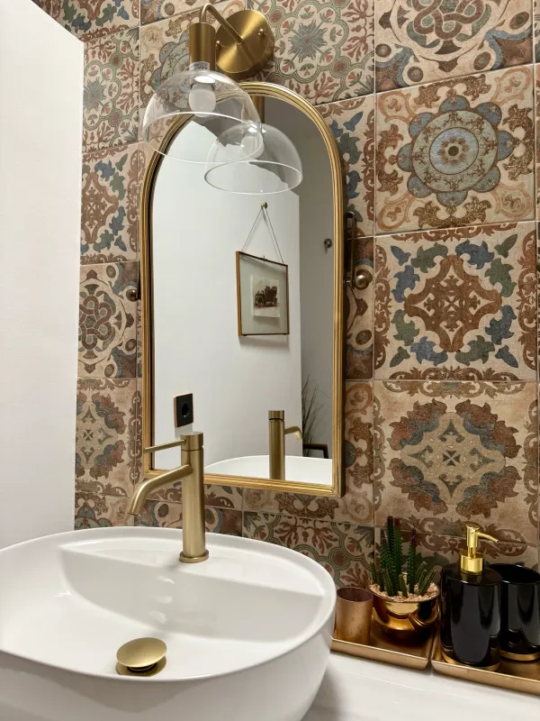 Baño con azulejos hidráulicos y espejo arqueado dorado
