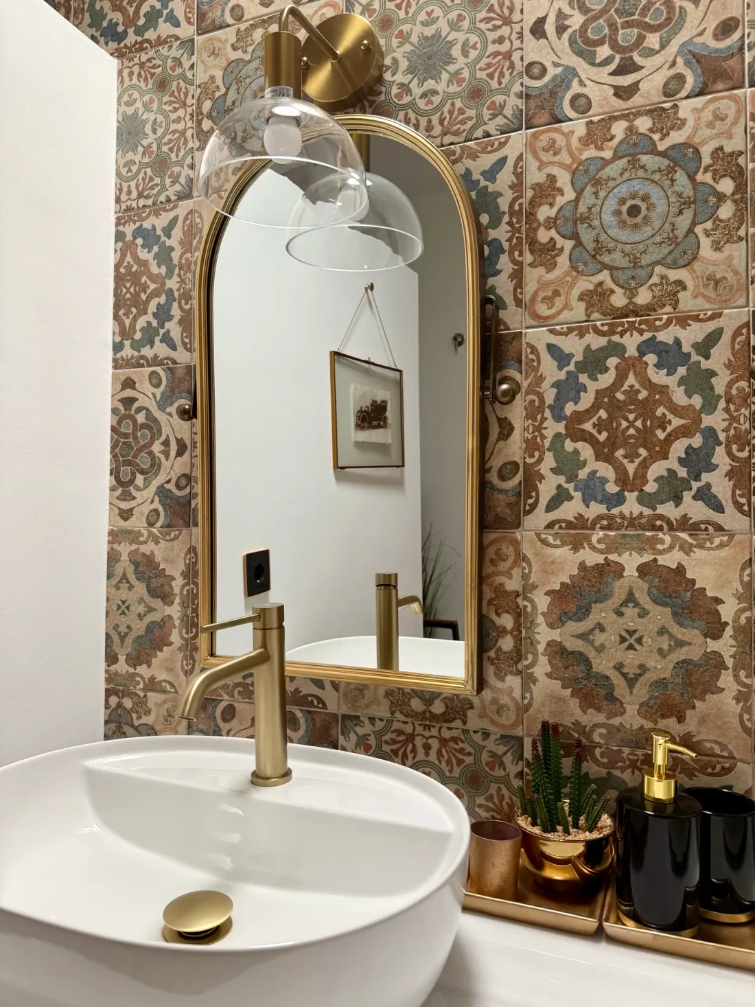 Baño con azulejos hidráulicos y espejo arqueado dorado