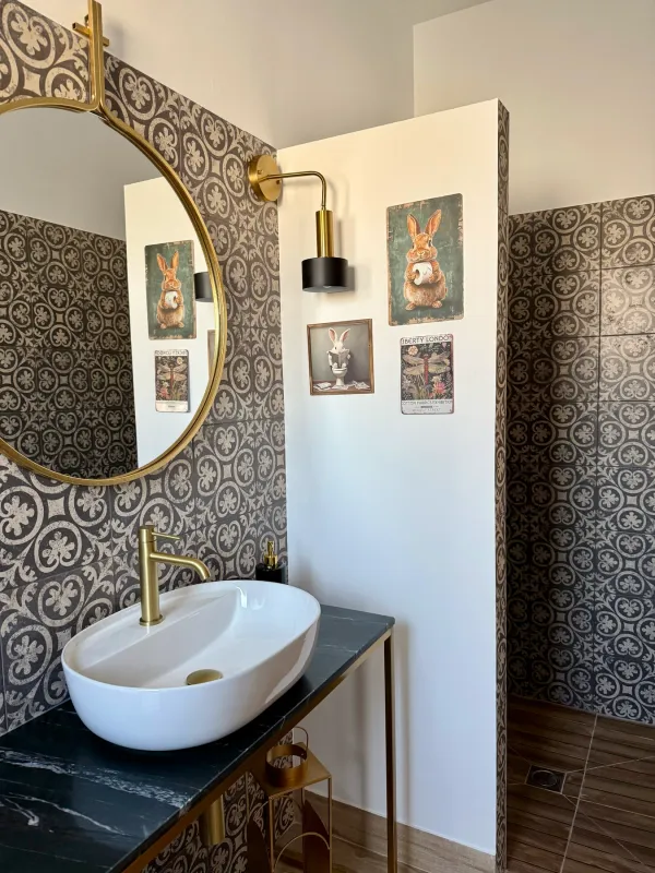 Baño con espejo redondo dorado y lavabo sobre encimera negra