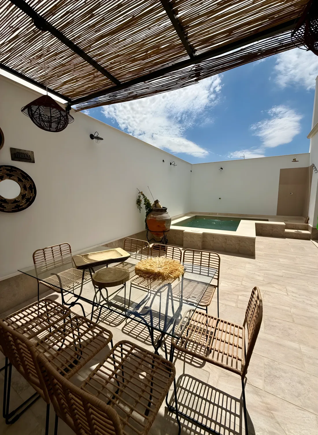 Patio con mesa de mimbre y cristal bajo una pérgola